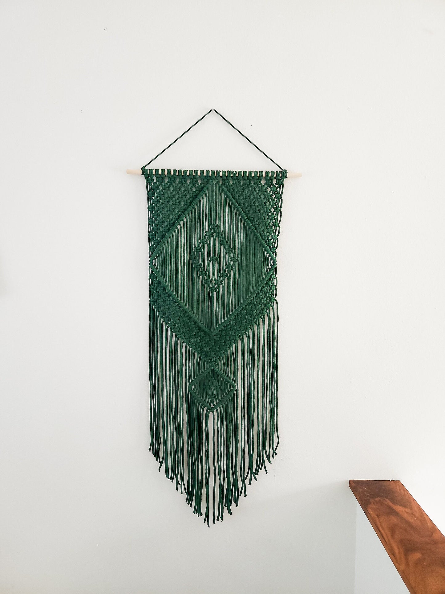 Green macrame wall hanging, hanging on a white wall.