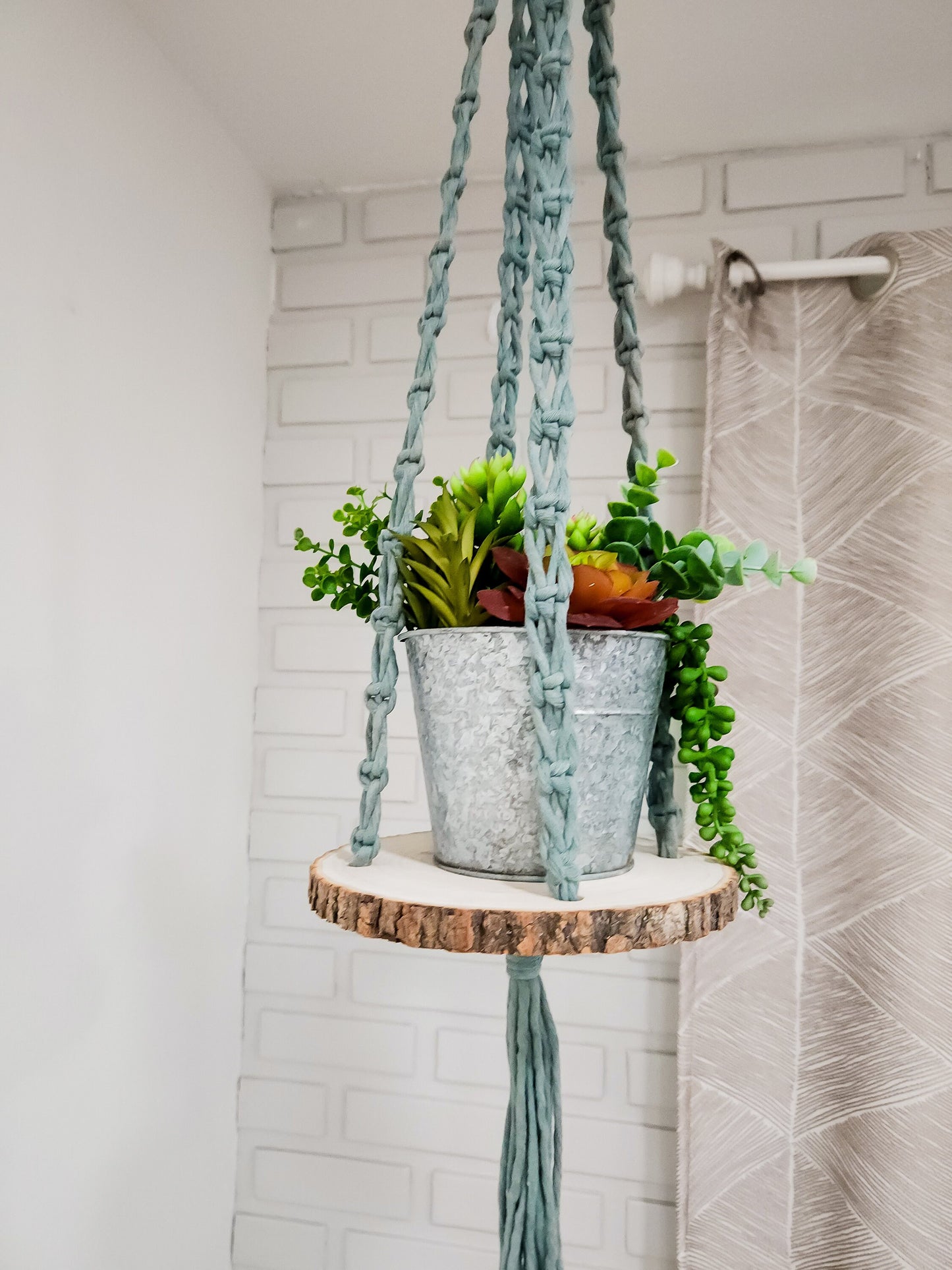 Macrame hanging shelf. It comes in a variety of cord colors, and it has a wood round with bark on the sides.