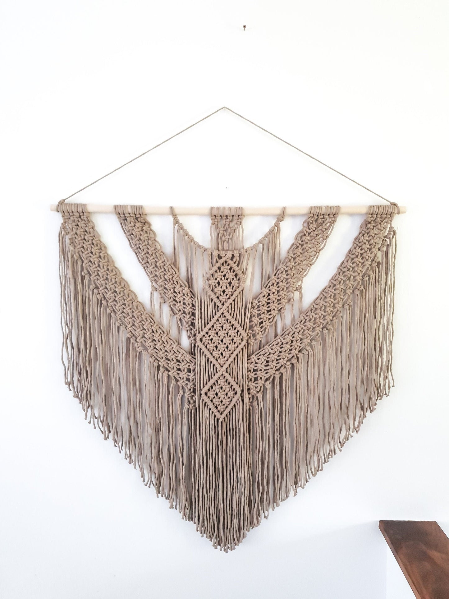 Light brown macrame wall hanging, it is 3 feet wide and 3 feet long. It is on a wood rod.