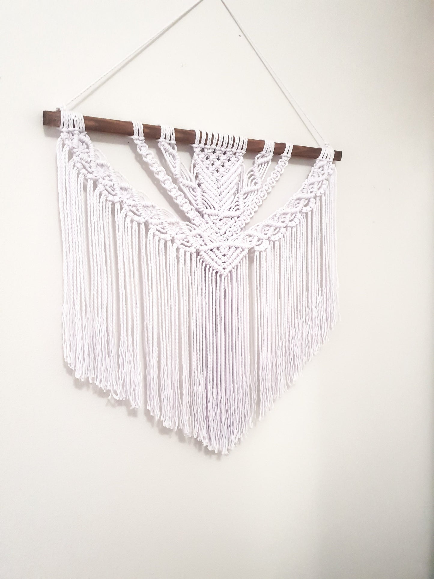 Pure white macrame wall hanging on a dark walnut stained wood stick.
