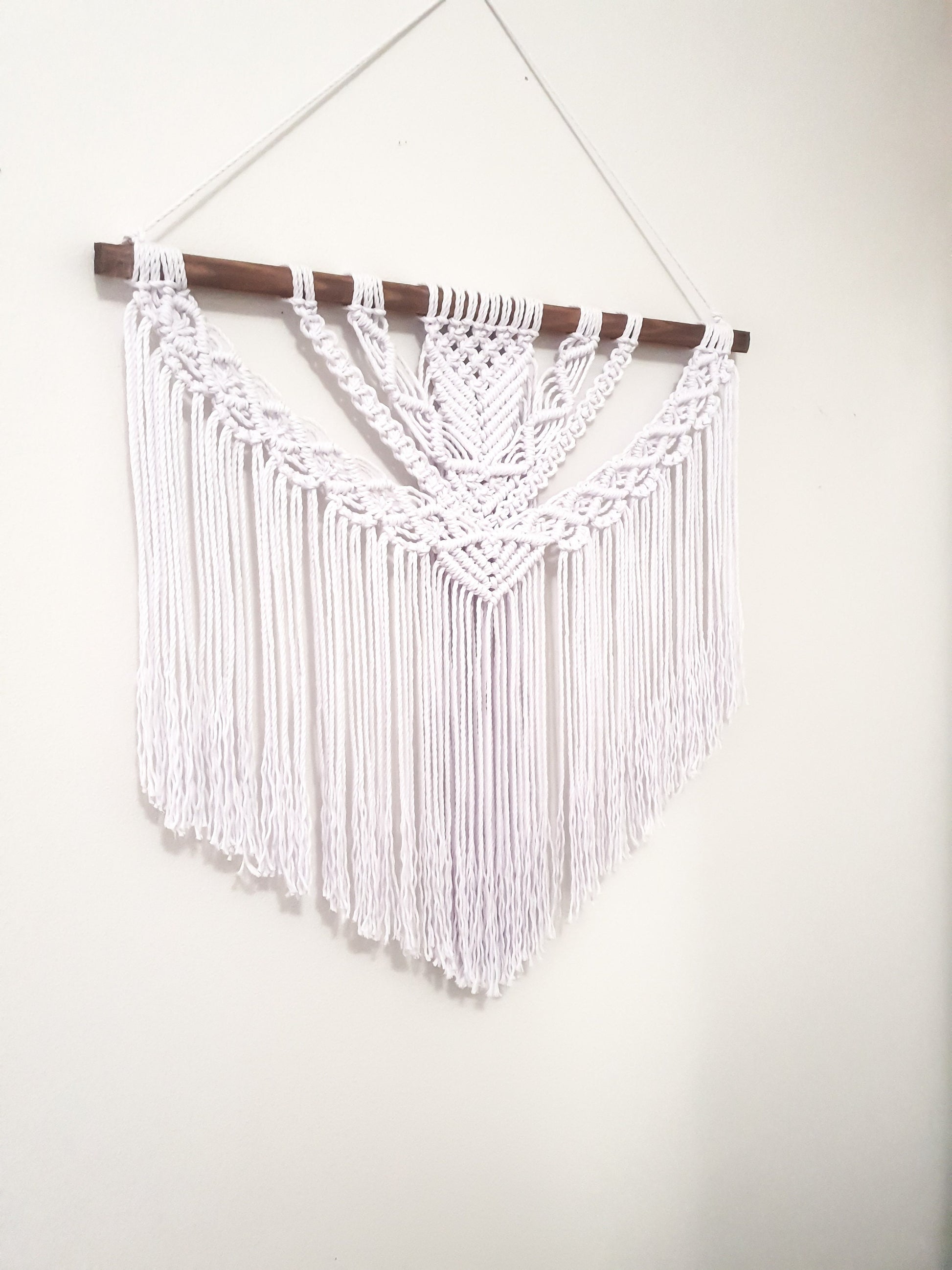 Pure white macrame wall hanging on a dark walnut stained wood stick.