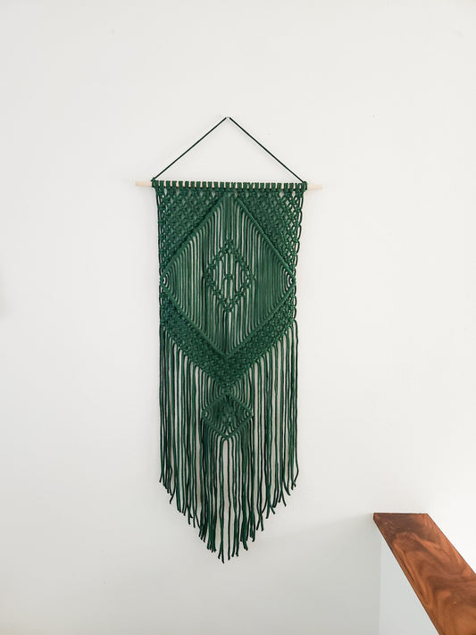 Green macrame wall hanging, hanging on a white wall.