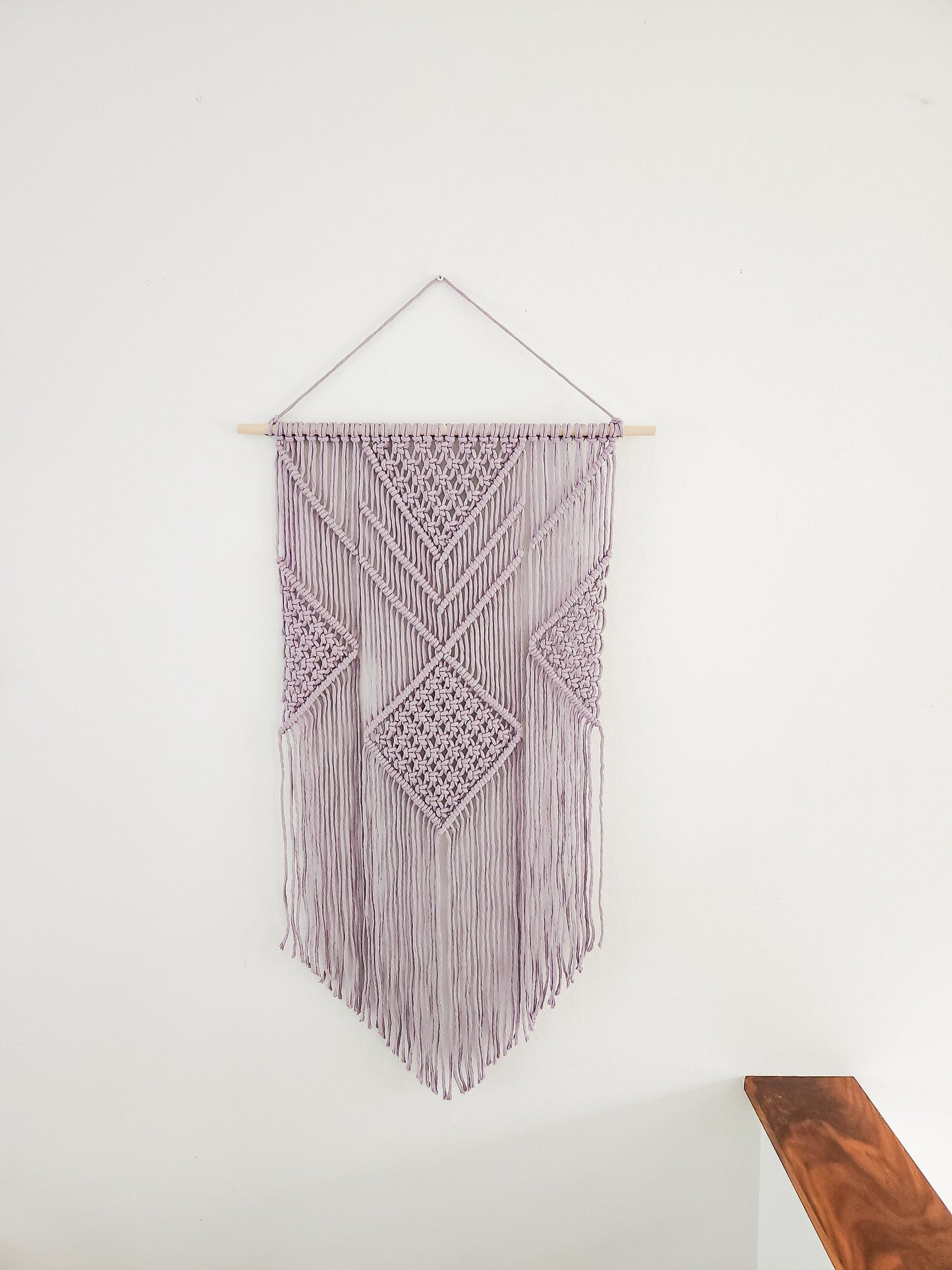 Lavender purple macrame wall hanging on a white wall.