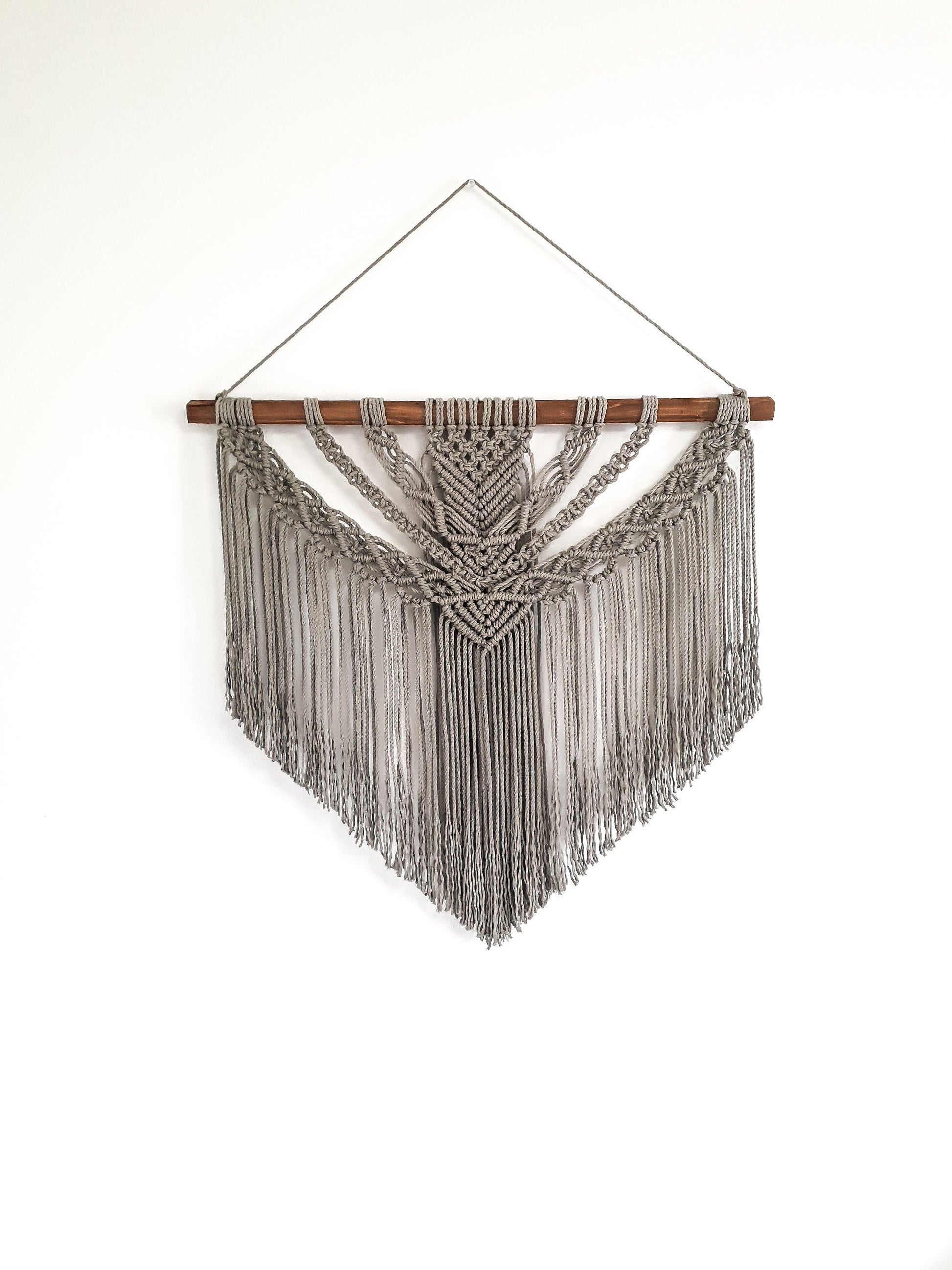Gray macrame wall hanging, on a dark walnut stained wood stick.