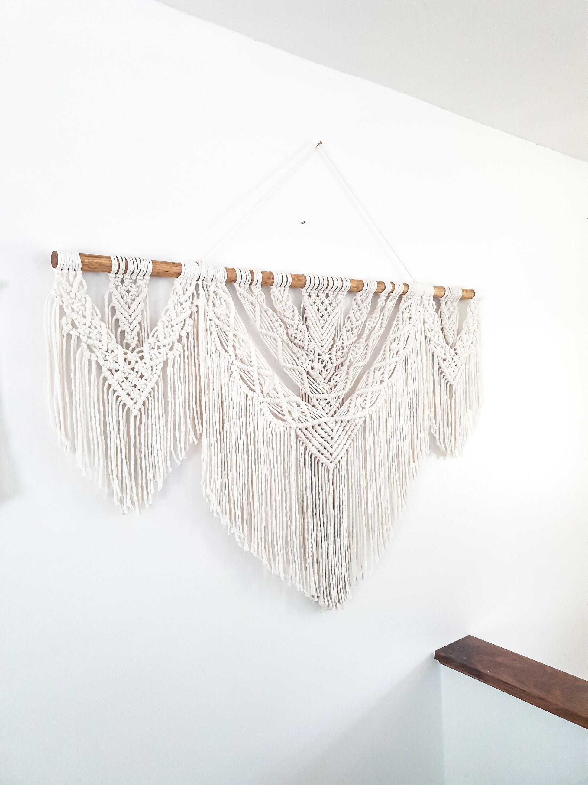 Beige (off white) 4 foot wide macrame wall hanging. It is made in 3 sections (larger middle section and smaller side sections) and it is on a piece of dark walnut stained wood rod.