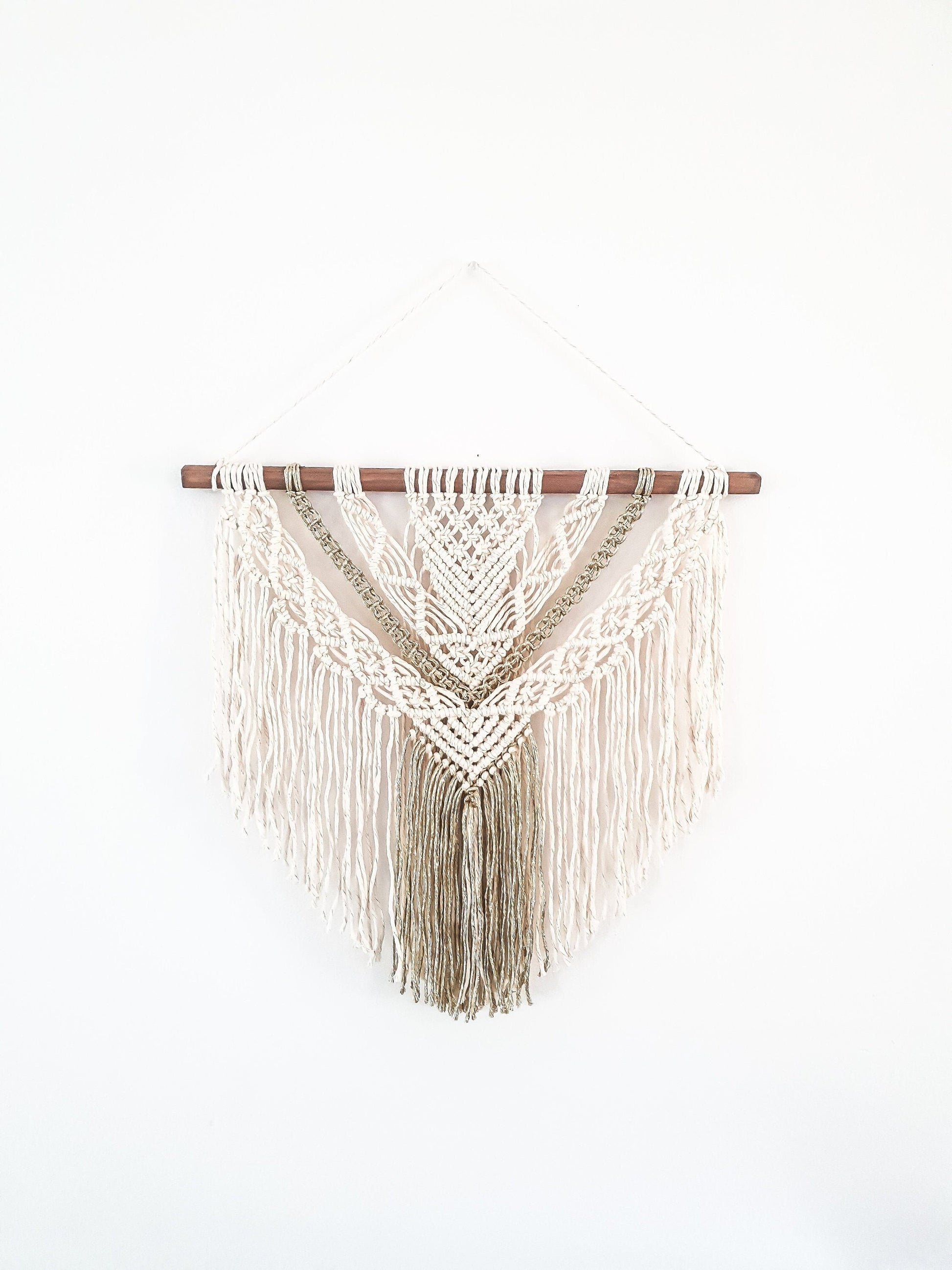 Beige and gold macrame wall hanging on a dark walnut stained wood stick.