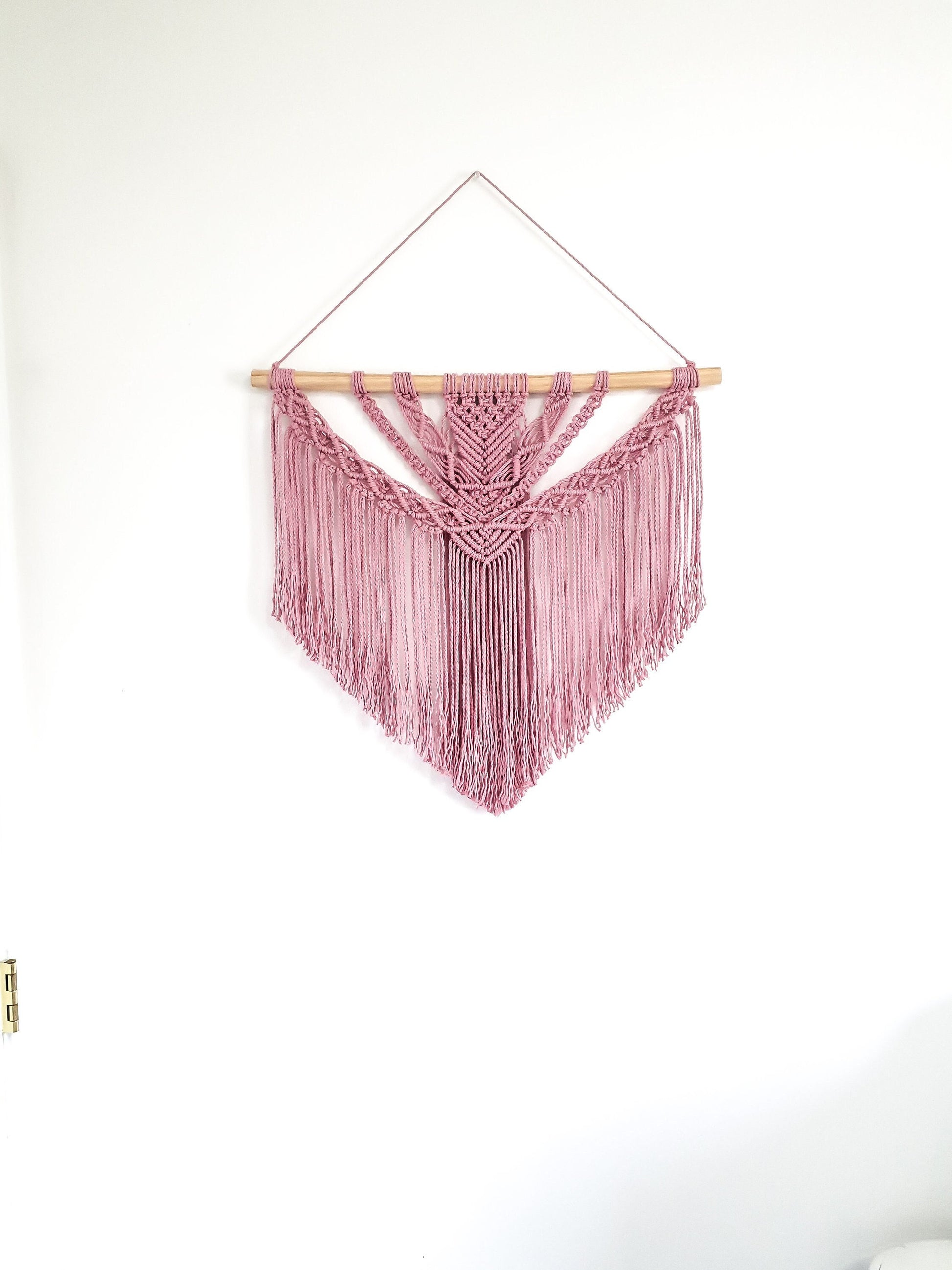 Pink macrame wall hanging on a piece of wood. There are 2 wood options, light colored wood and dark stained wood.