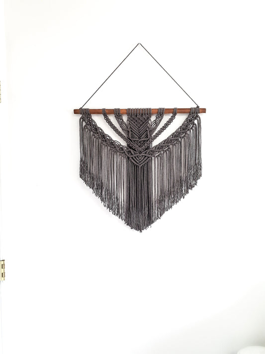 Dark gray macrame wall hanging on a piece of dark walnut stained wood.